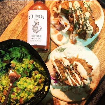 Soft tacos with chilli mayo next to a guacamole bowl with a bottle of Old Bones Chilli Co: Smoked Chilli Garlic sauce