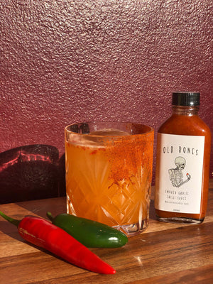 Cocktail recipe | Mexican firing squad cocktail in a short glass next a bottle of Old Bones Chilli Co Smoked Garlic Chilli Sauce