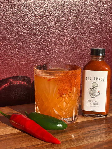 Cocktail recipe | Mexican firing squad cocktail in a short glass next a bottle of Old Bones Chilli Co Smoked Garlic Chilli Sauce