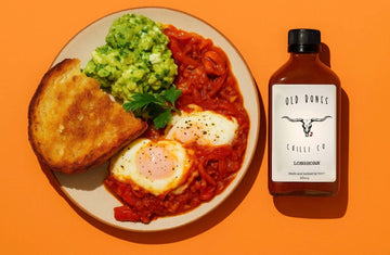 Recipe - Spicy Shakshuka with Feta & Avocado Salad on a bowl nect to a bottle of Old Bones Chilli Co Smoked Garlic Chilli sauce