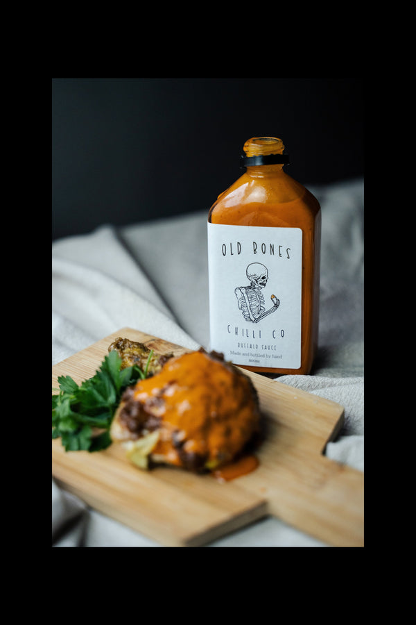 Bottle of Old Bones Chilli Co Buffalo Sauce on a wooden board with food