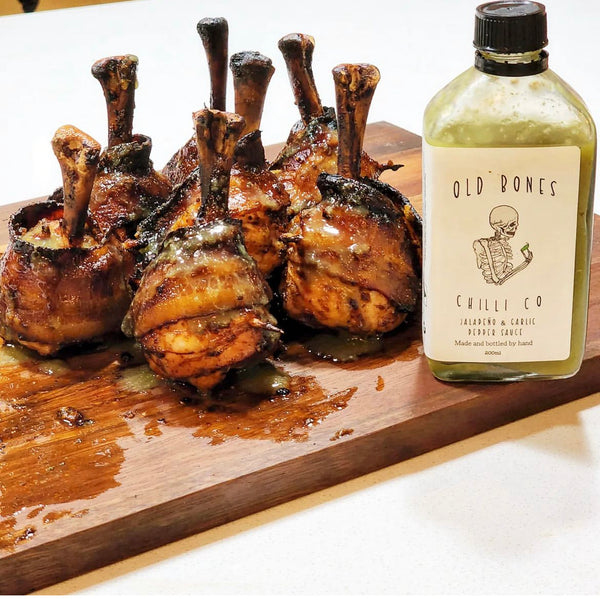 Wooden board with roasted lamb cutlets and a bottle of Old Bones Chilli Co sauce.